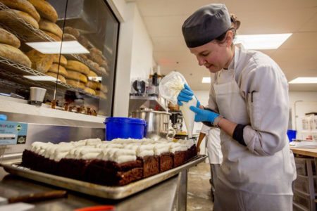 Crust employee Jill Davis, 29, of Owosso squeezes whip cream on a Michigan staple, Bump Cake, on Friday, Feb. 23, 2018 at Crust Bakery in Fenton
