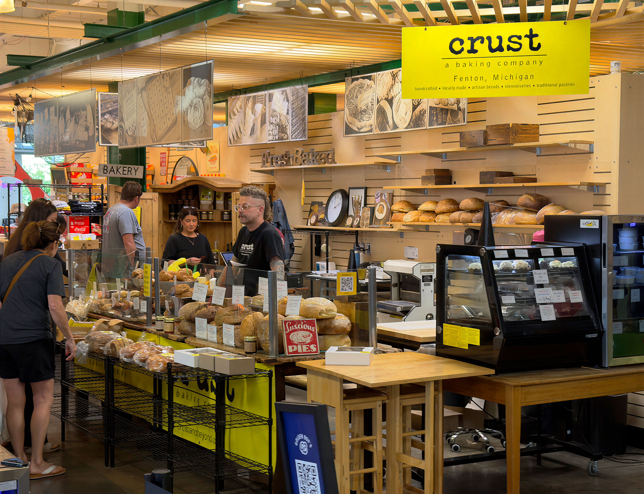 The CRUST bakery counter at the Flint Farmers' Market, with loaves on the shelves and the yellow CRUST sign