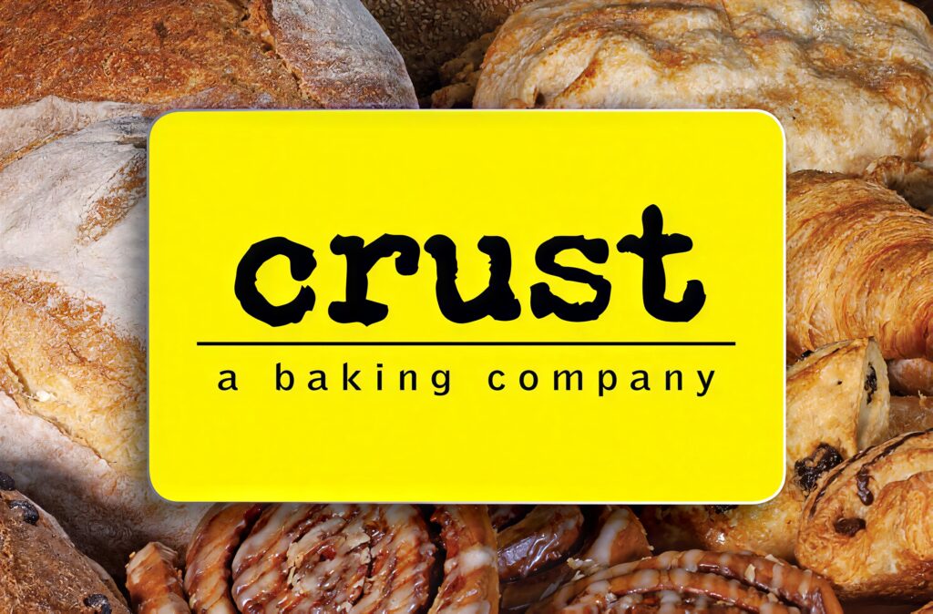 The yellow CRUST gift card on a spread of fresh bread, croissants and cinnamon rolls