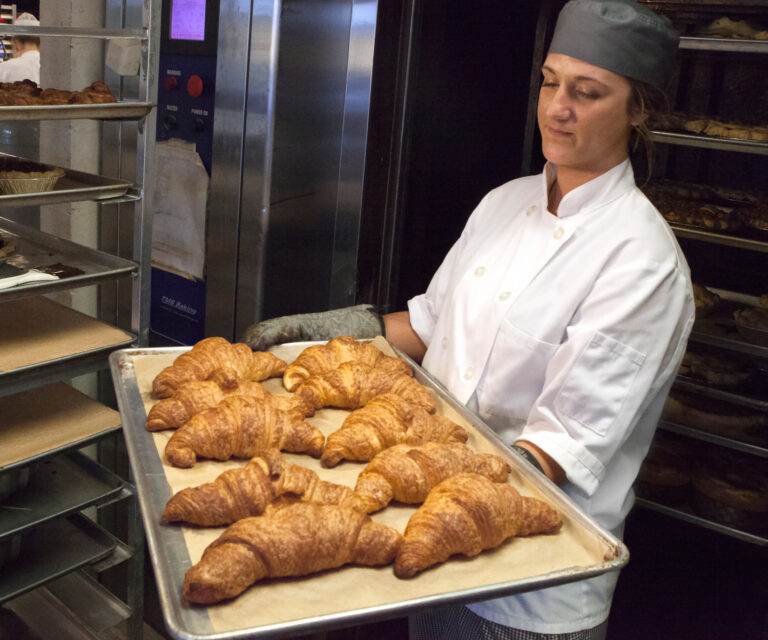 A CRUST baker pulling a tray of golden butter croissants from the oven