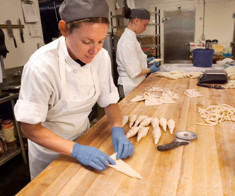 CRUST bakers hand-rolling croissants at a long wooden bench