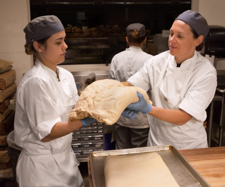 Two CRUST bakers passing a large piece of laminated dough between them