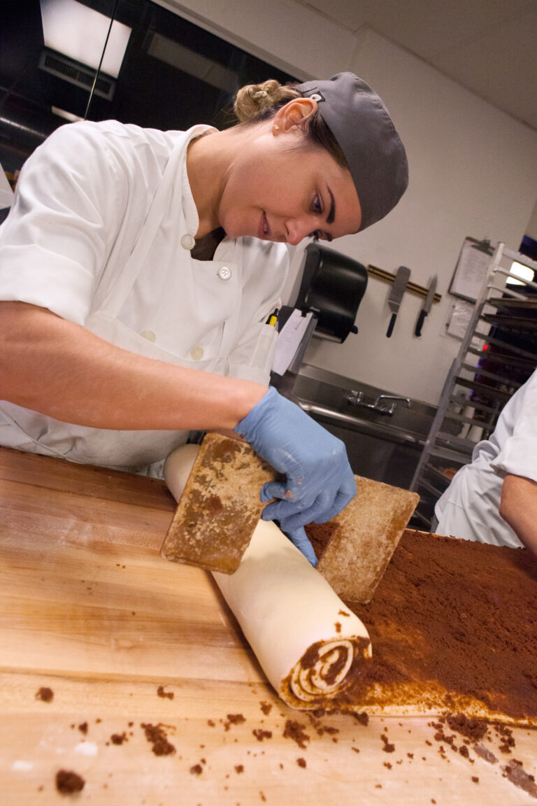 A CRUST pastry baker rolling up a sheet of cinnamon roll dough