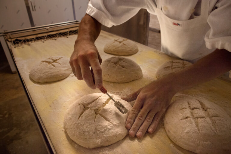 A baker scoring round loaves of bread by hand before they go into the oven