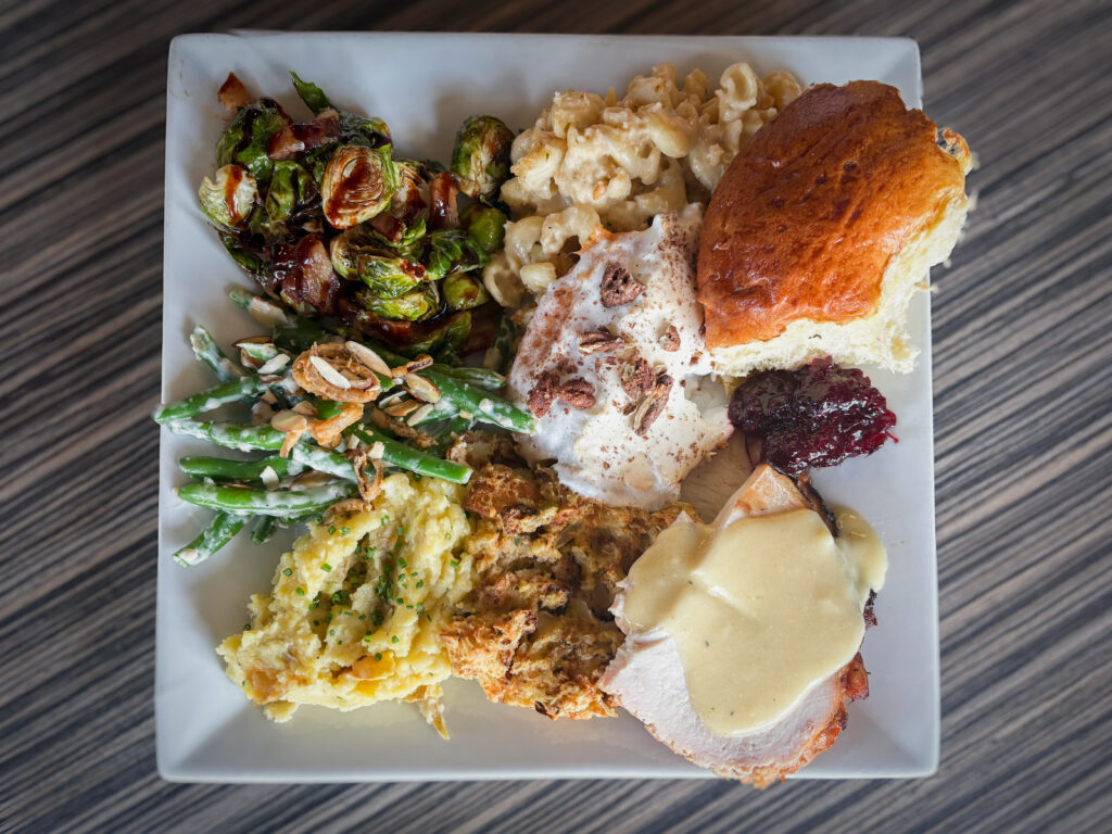 A plate of CRUST Thanksgiving dinner: roasted turkey with gravy, stuffing, mashed potatoes, green beans, Brussels sprouts, mac and cheese, yams, cranberry preserves and a sweet roll